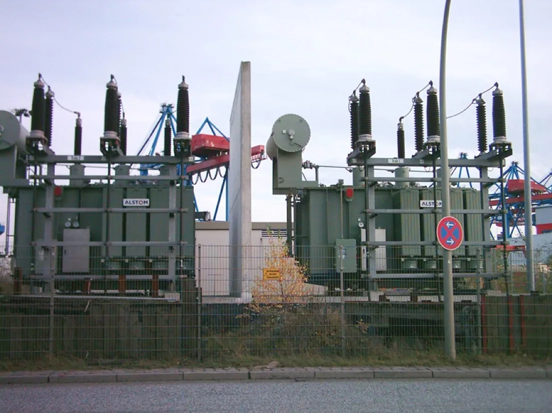 Two large substation transformers behind a fence, with insulators and high-voltage connections.