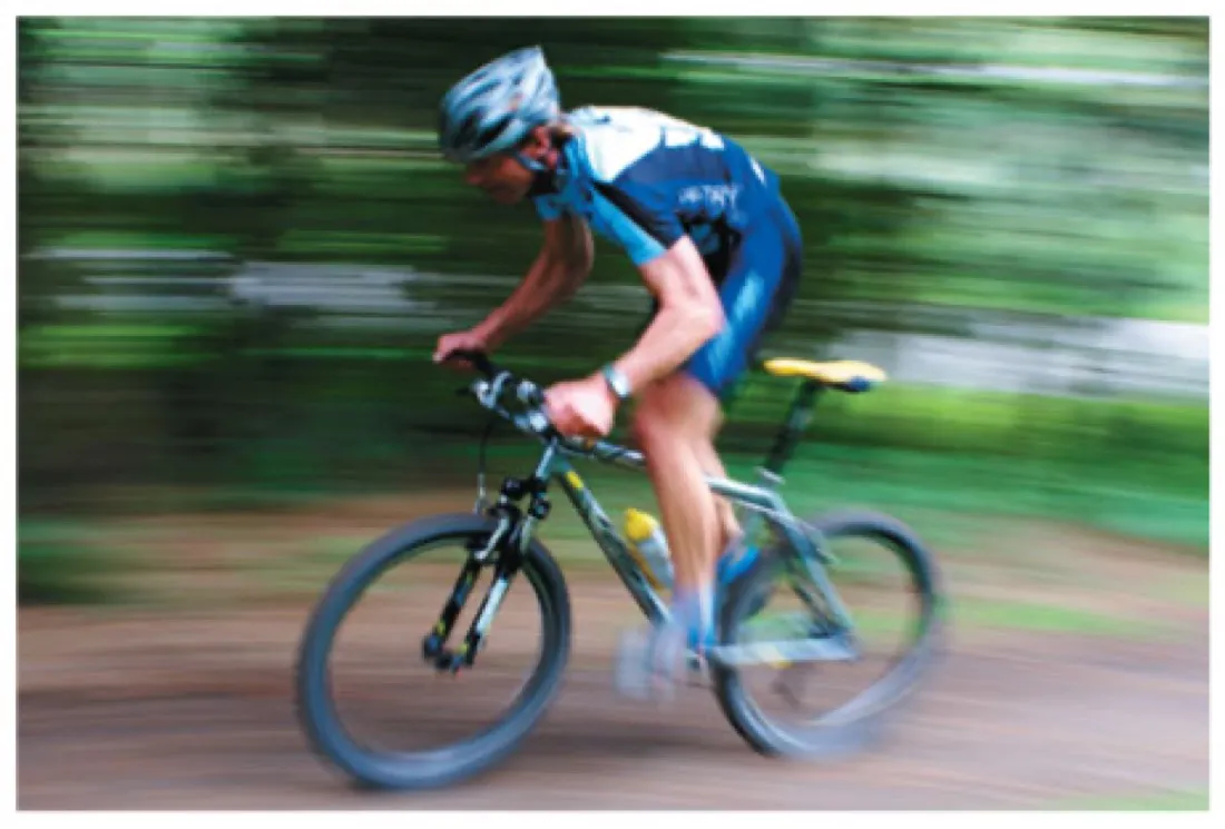 Photograph of a mountain biker sharply in focus against a heavily motion-blurred green background