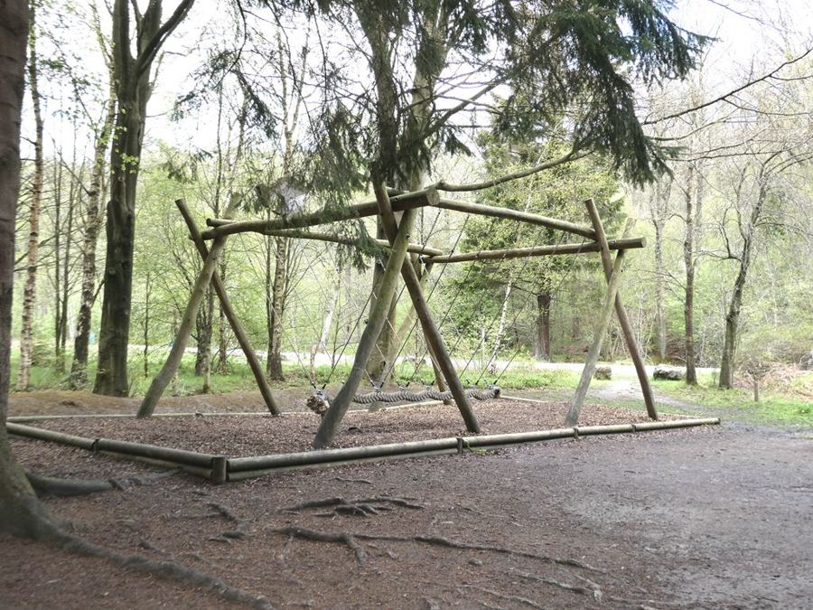 A large wooden multi-seat swing frame in a woodland playground