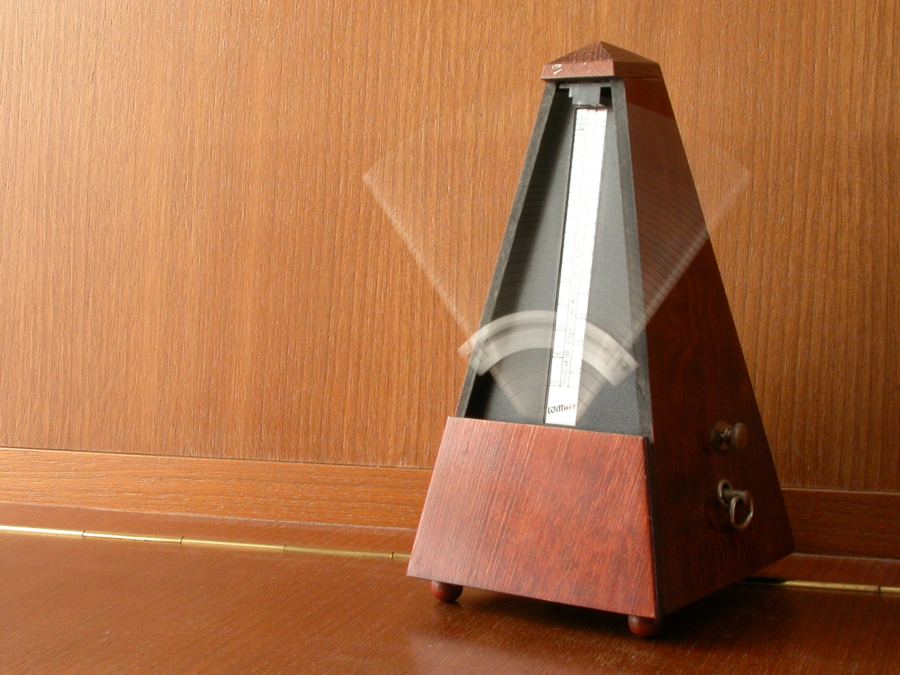 A wooden pyramid metronome with its pendulum arm swinging