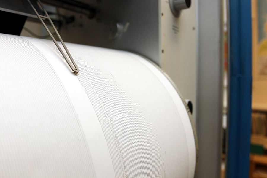 A seismometer pen resting on a rotating paper drum covered in fine traces