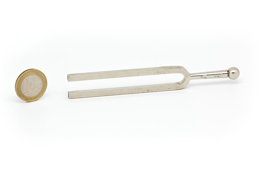 A steel tuning fork marked 440 Hz lying beside a coin